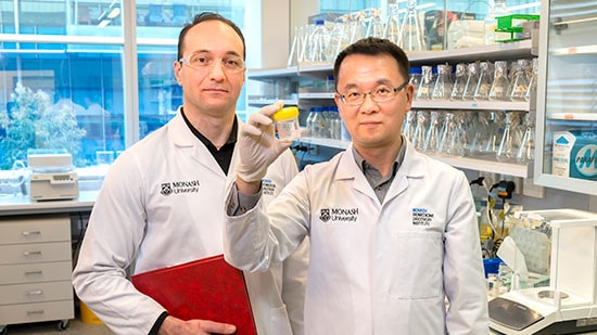 Two men in white lab coats stand in a science lab 