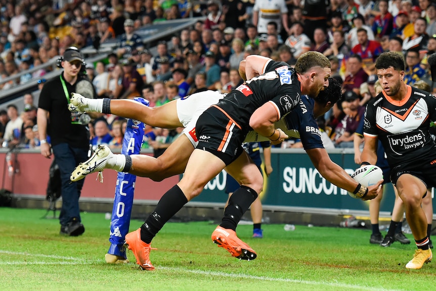 North Queensland Cowboys' Murray Taulagi is tackled over the sideline by Wests Tigers' Jackson Hastings as he passes the ball.