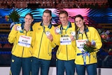 Four Australian swimmers, two female, two male, stand smiling on the podium with silver medals.