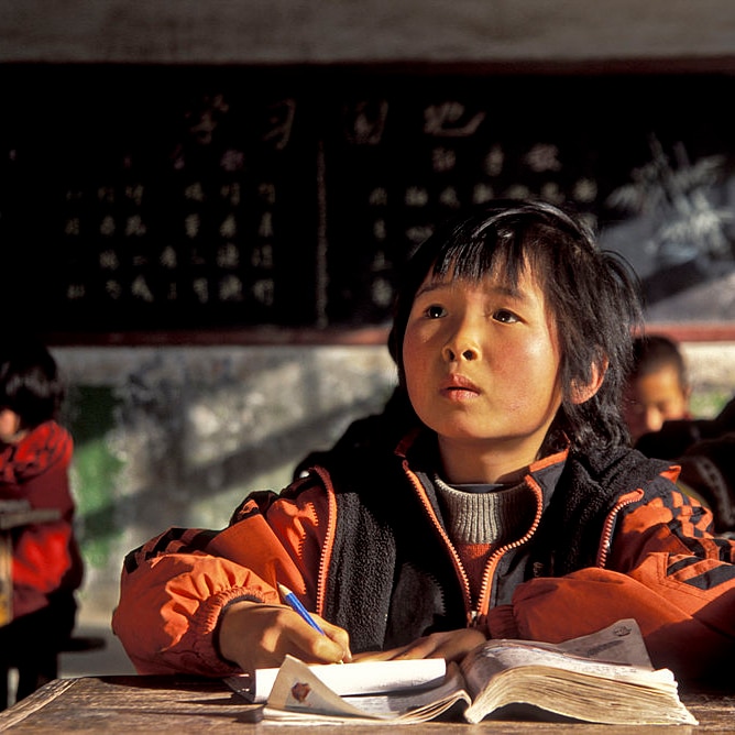 Chinese students at their desks in a classroom with one looking up.