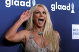 Singer Britney Spears is laughing and waving on a red carpet