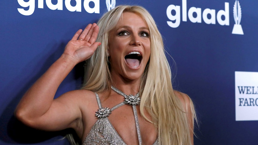 Singer Britney Spears is laughing and waving on a red carpet