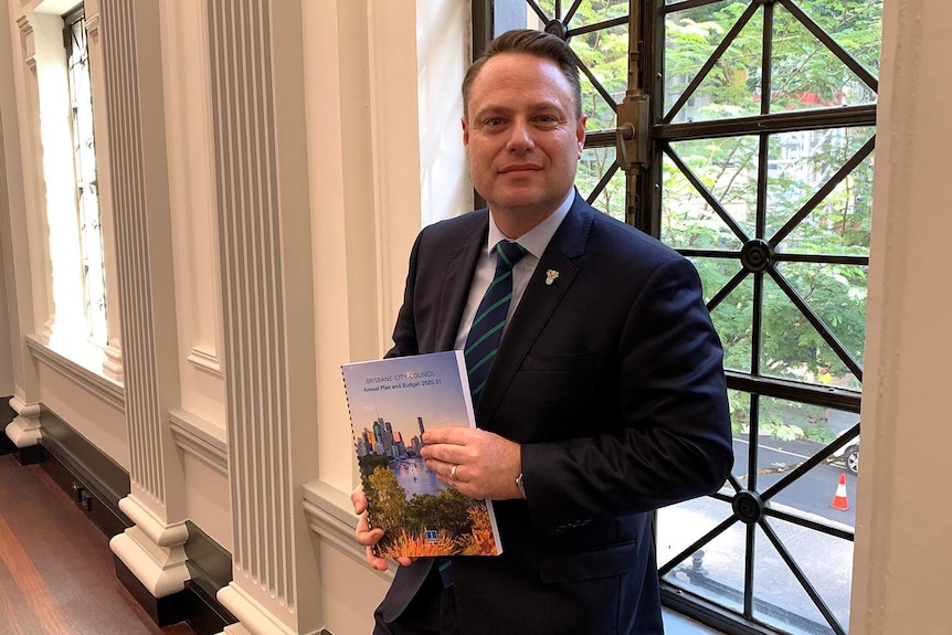 Brisbane Lord Mayor Adrian Schrinner stands in City Hall holding onto the Council's budget document.