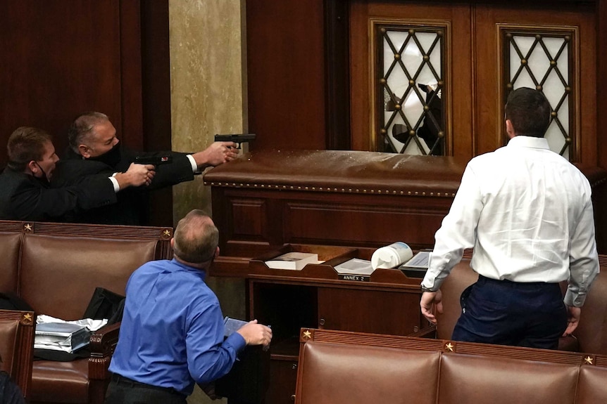 Police with guns drawn watch as protesters try to break into the House Chamber at the US Capitol