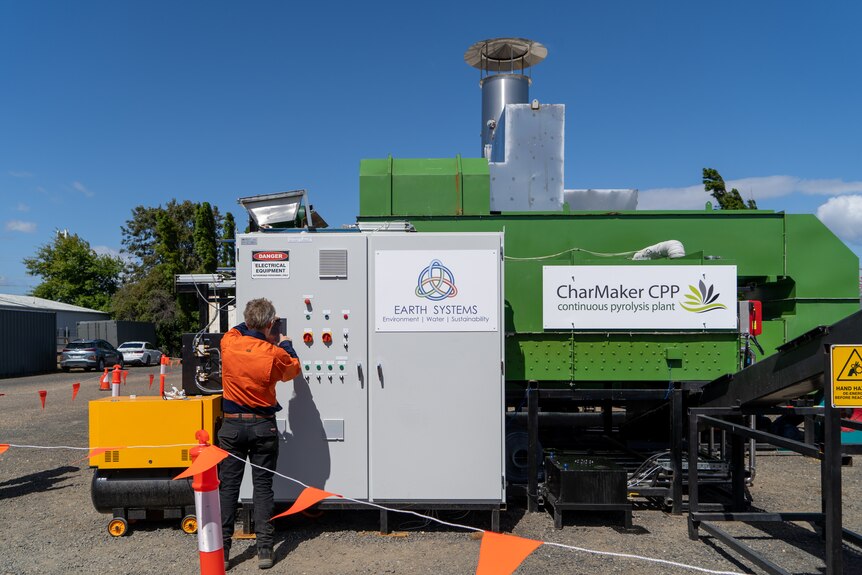 A green and grey metal pyrolysis technology machine in Sale, with a person in high vis standing near it operating the controls.