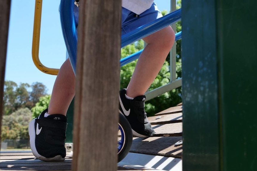 A little boy with cerebral palsy tries to run up a ramp on a playground