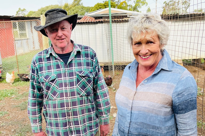 Man and woman smiling and standing outdoors in a chicken enclosure. 