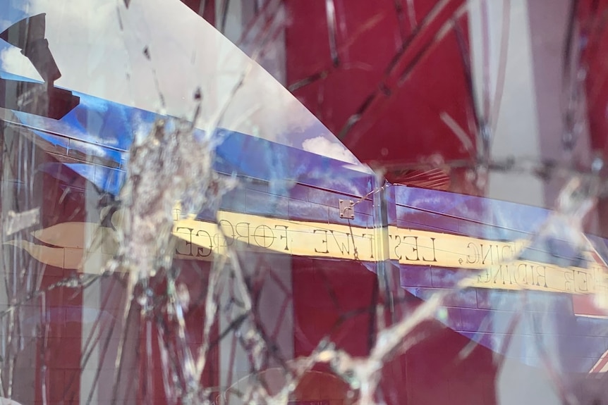 Smashed glass with a mural depicting the words Lest We Forget reflected in the shattered glass.