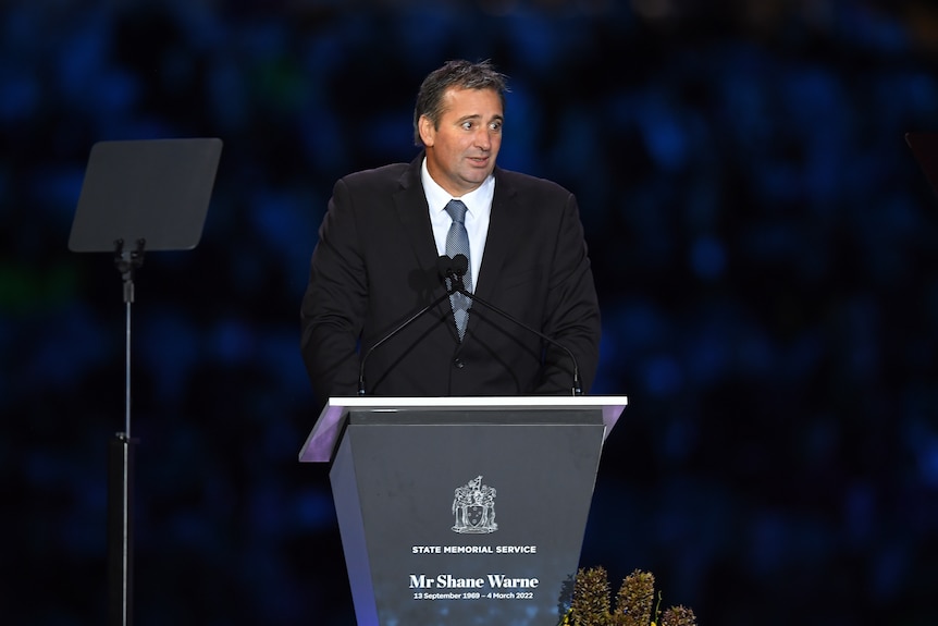 A man wearing a suit standing at a lectern on a stage.