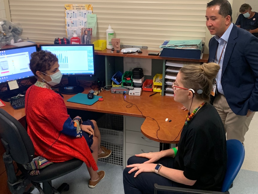 Dr Dayse Tavora-Vieira sits at a desk with Hannah as Dr Jafri Kuthubutheen observes