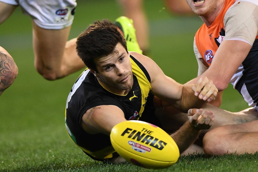 Trent Cotchin looks at the ball while laying on the ground.