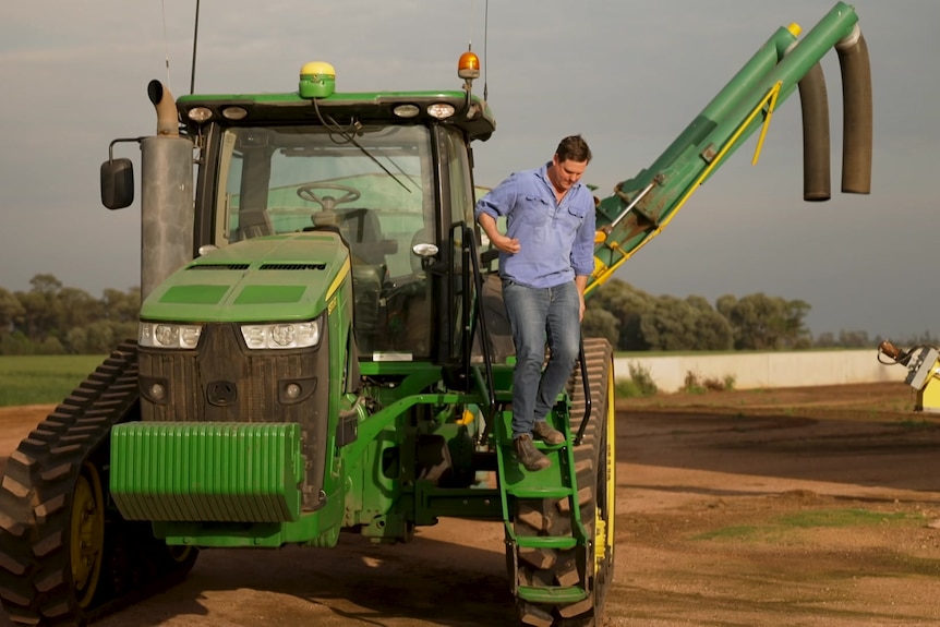 Photo of a man stepping off a tractor.