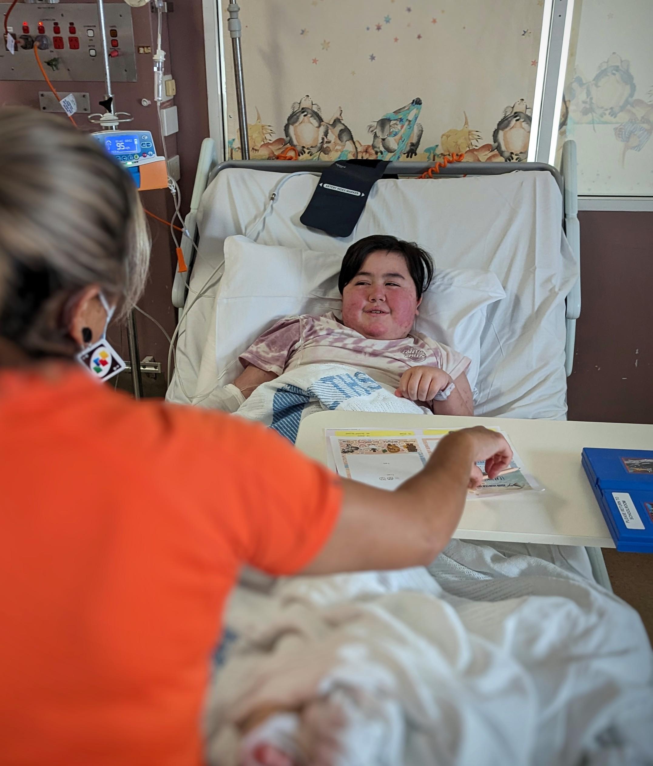 A teacher conducting a lesson with Payton Allen in her hospital bed.