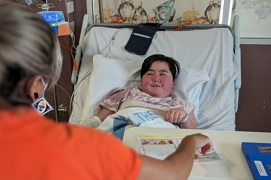 A teacher conducting a lesson with Payton Allen in her hospital bed.