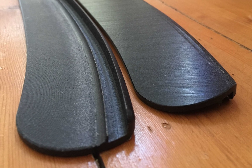 A black piece of curved plastic sits on a wooden surface