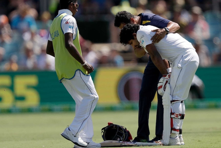 Medical staff attend to Kusal Perera, who is bent over with his helmet on the ground.