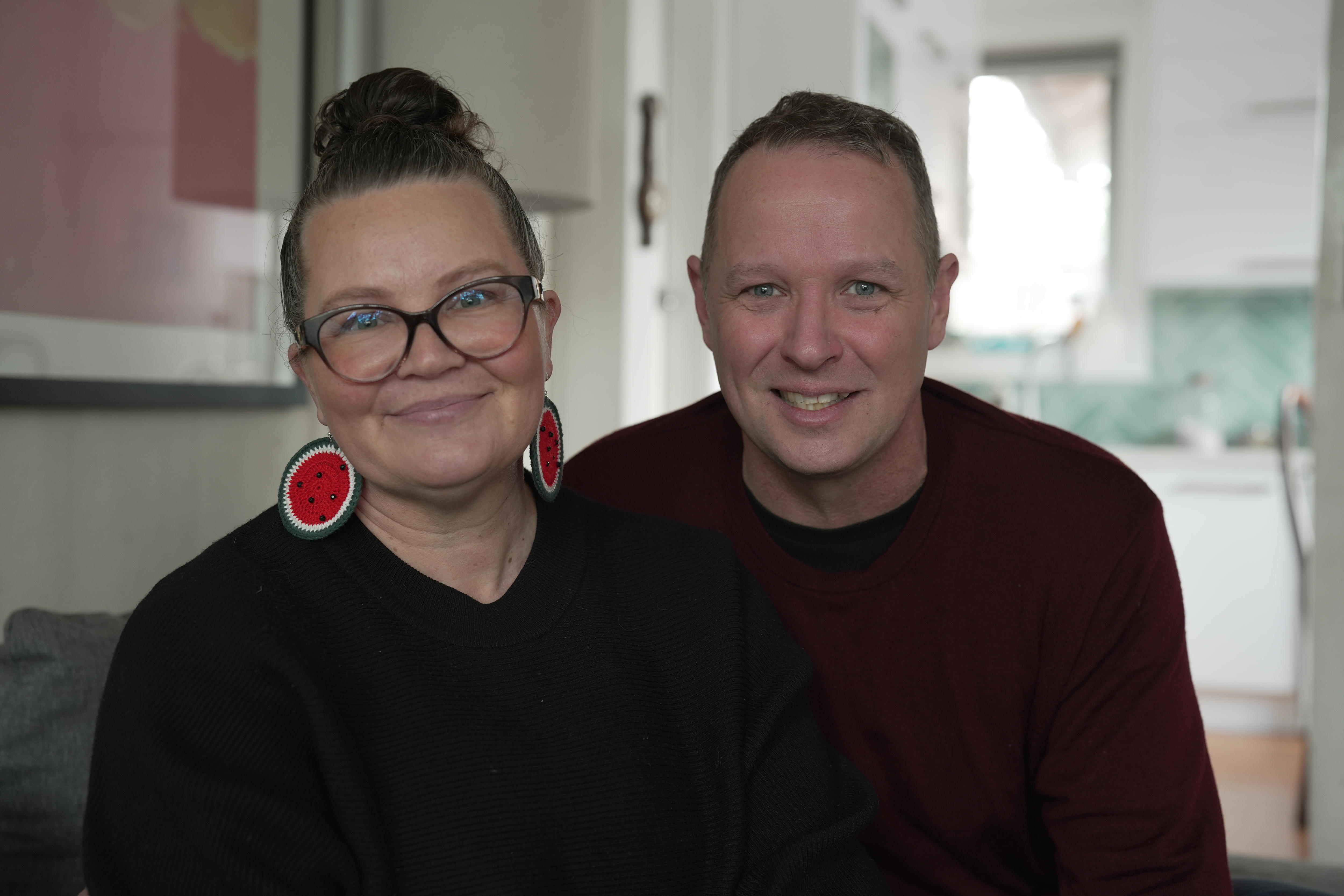 A white man and white woman sitting in a kitchen looking at the camera
