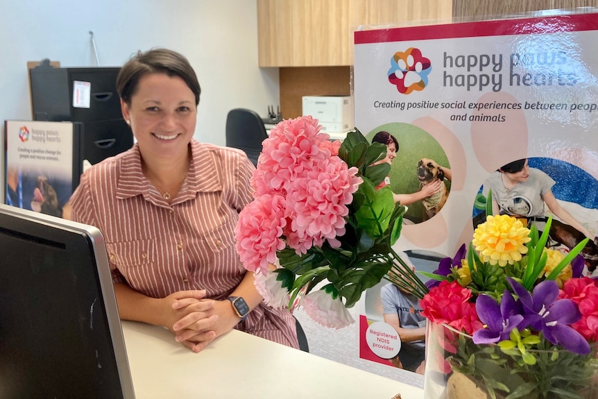 A woman beside flowers and signage.