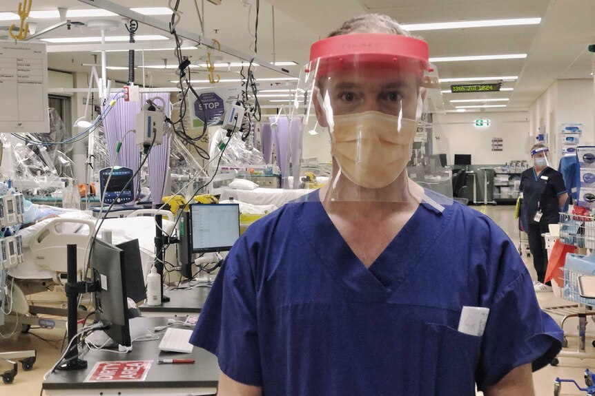 Forbes McGain, intensive care physician, standing in ICU wearing visor and protective mask.