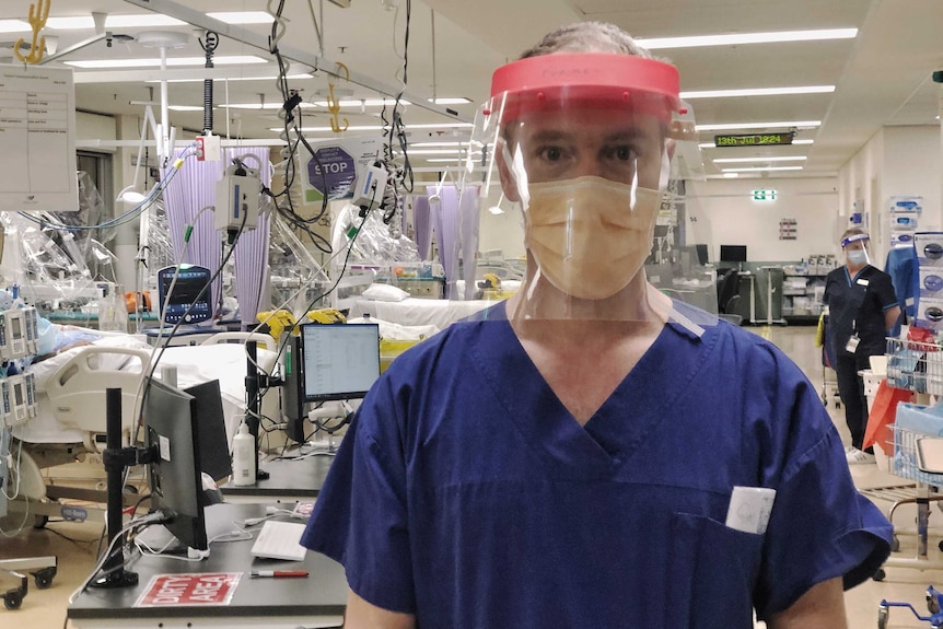 Forbes McGain, intensive care physician, standing in ICU wearing visor and protective mask.