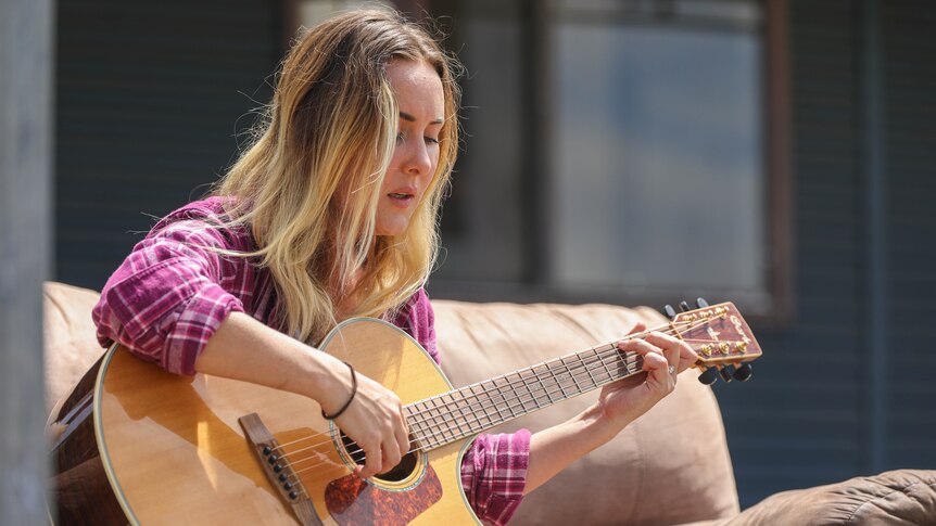 A young blonde woman sings and plays the guitar.