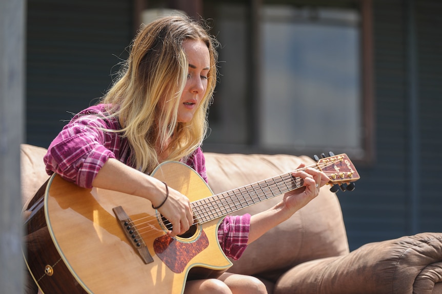 A young blonde woman sings and plays the guitar.