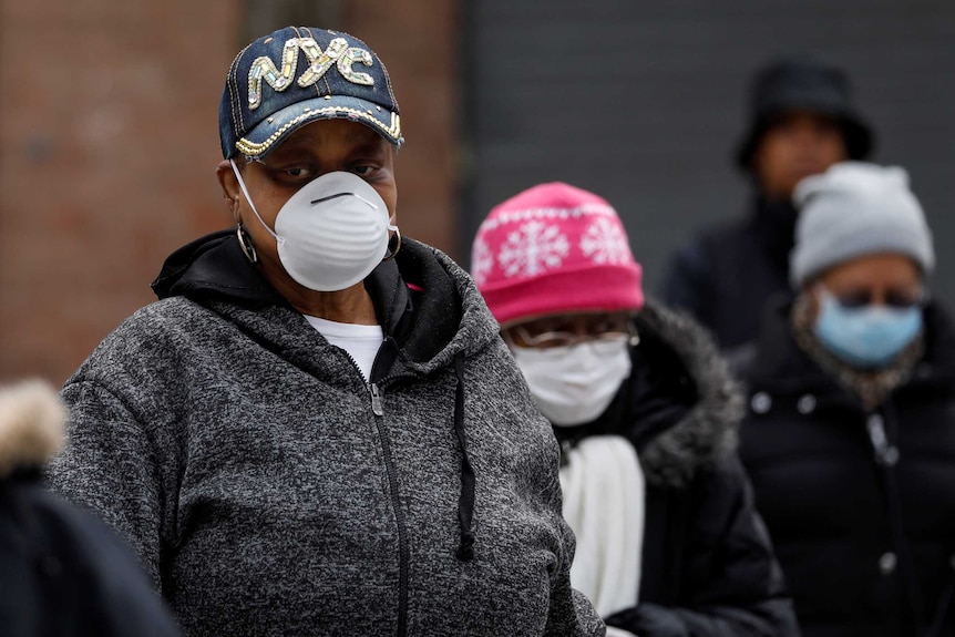 People in jumpers wearing face masks wait in line