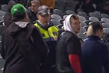 A television screenshot of a number of young men standing near a police officer, who is speaking to them