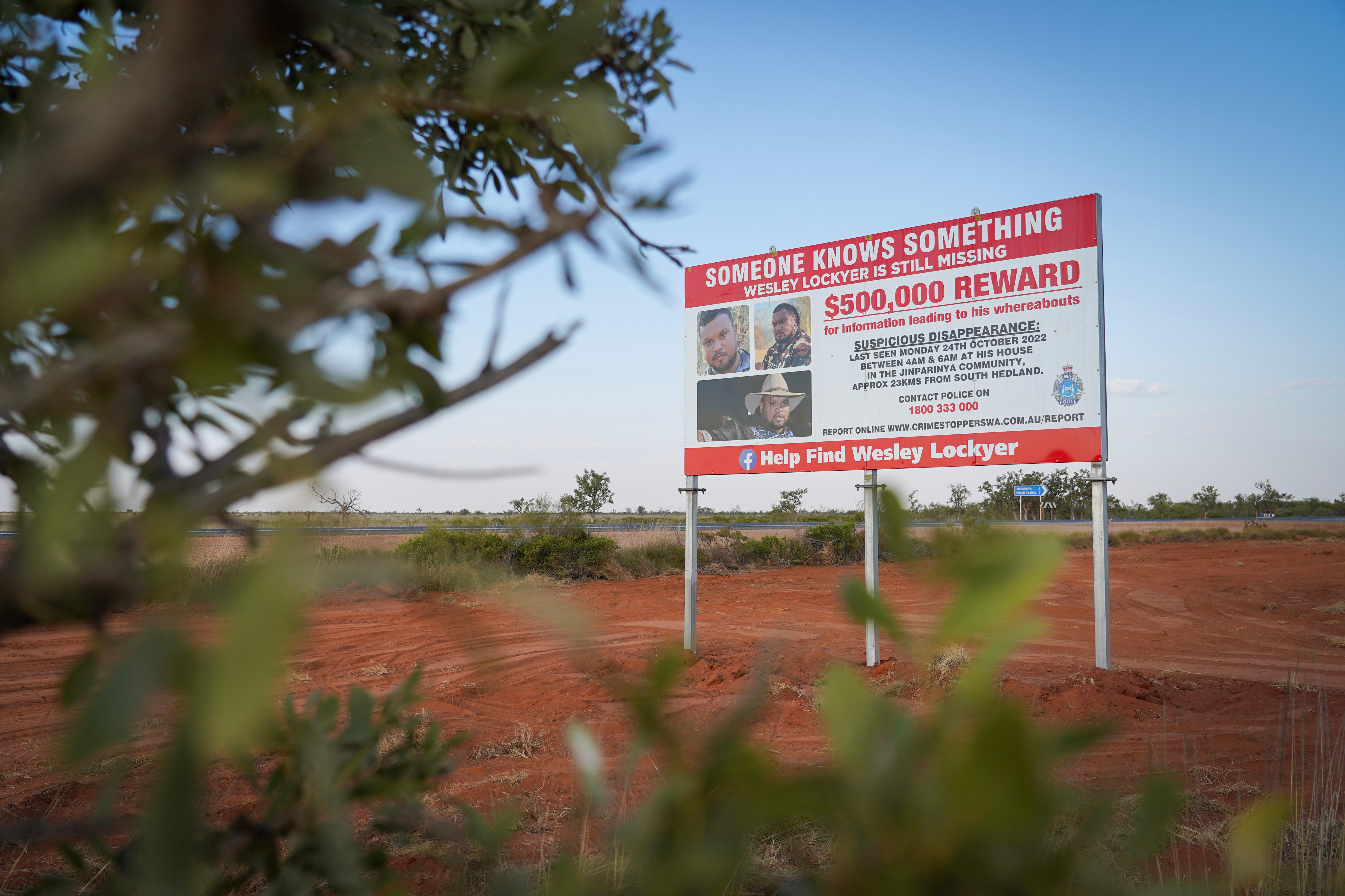 A billboard offering a reward for information about a missing person stands on the side of an outback road.