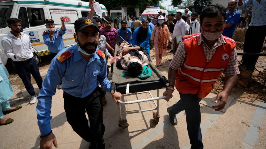 An injured man is wheeled on a stretcher by two men.