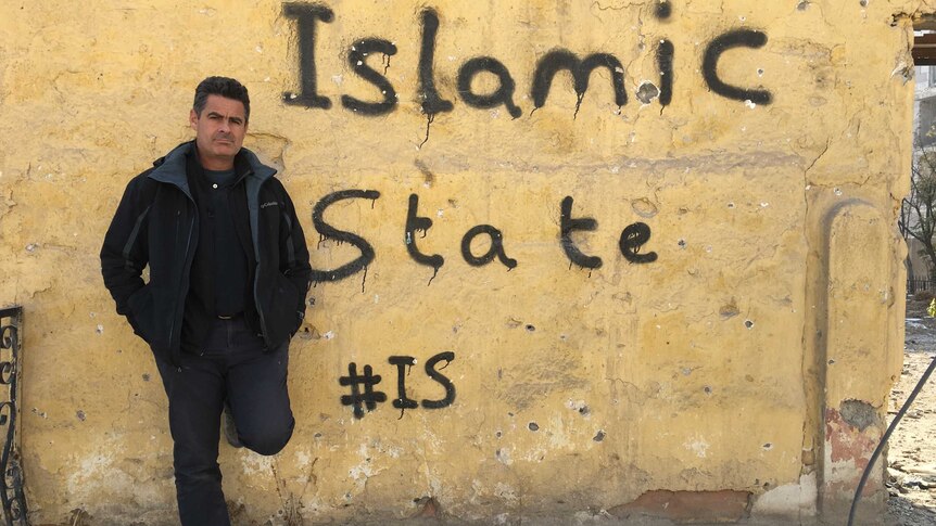 Matt Brown leaning against bullet-ridden wall painted with Islamic State #IS graffiti.