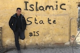Matt Brown leaning against bullet-ridden wall painted with Islamic State #IS graffiti.
