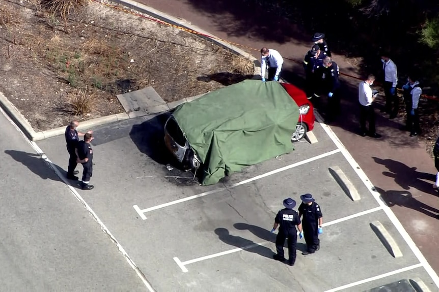 Police officers surround a partly covered car