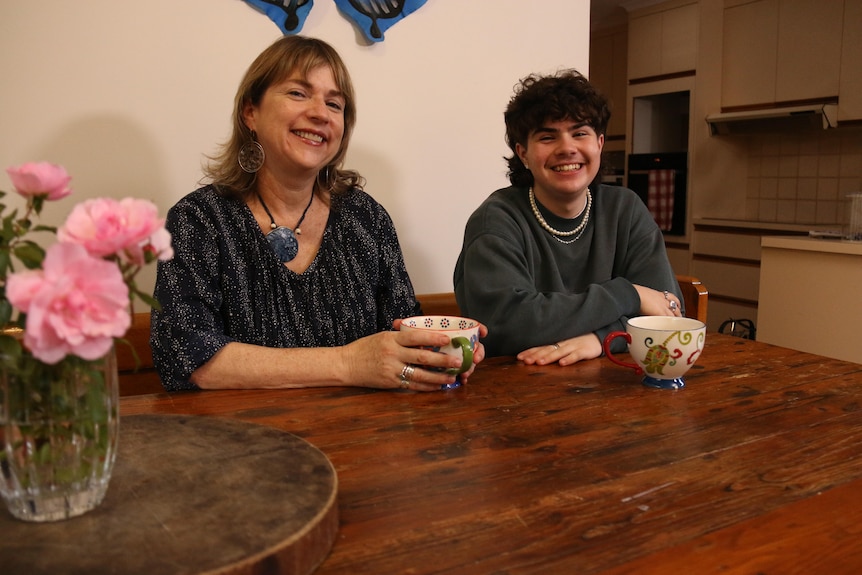 A middle aged woman sits at a table with a teenage boy.