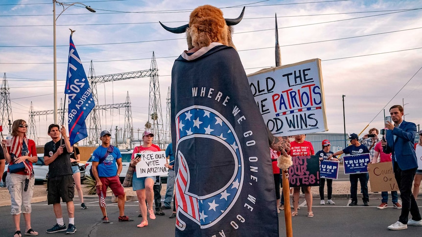A man wrapped in a QAnon flag addresses supporters of US President Donald Trump
