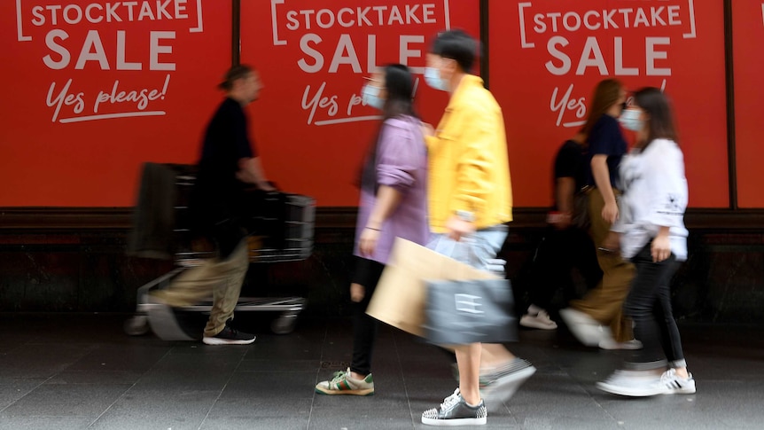 Shoppers, some wearing face masks, walk past a sign that says Myer Stocktake Sale.