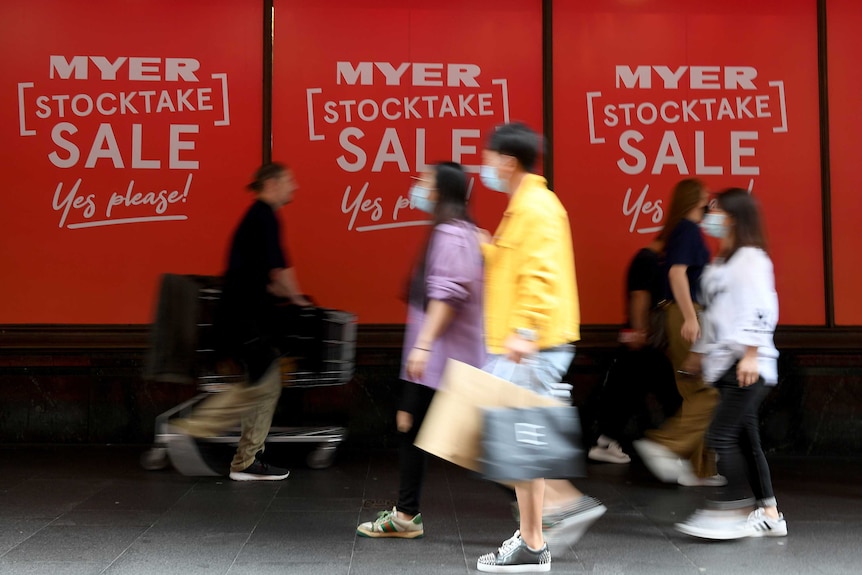 Shoppers, some wearing face masks, walk past a sign that says Myer Stocktake Sale.