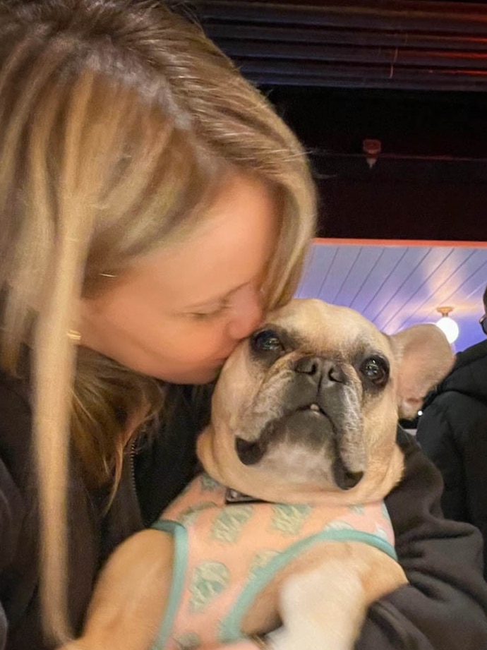 Woman with blonde hair kisses her fawn coloured French Bulldog in a bar