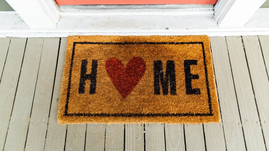 A brown front door mat at the entrance to a house reads 'HOME'