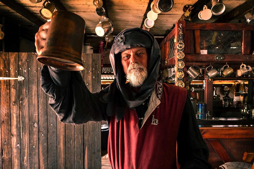 A man in medieval clothing toasts with a beer mug in a beer hall.