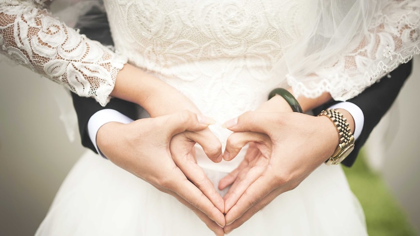 A bride and groom make a heart shape with their hands.