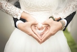 A bride and groom make a heart shape with their hands.