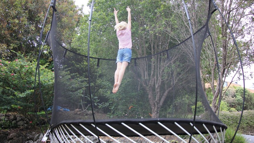 A child jumping on a round trampoline surrounded by a net.