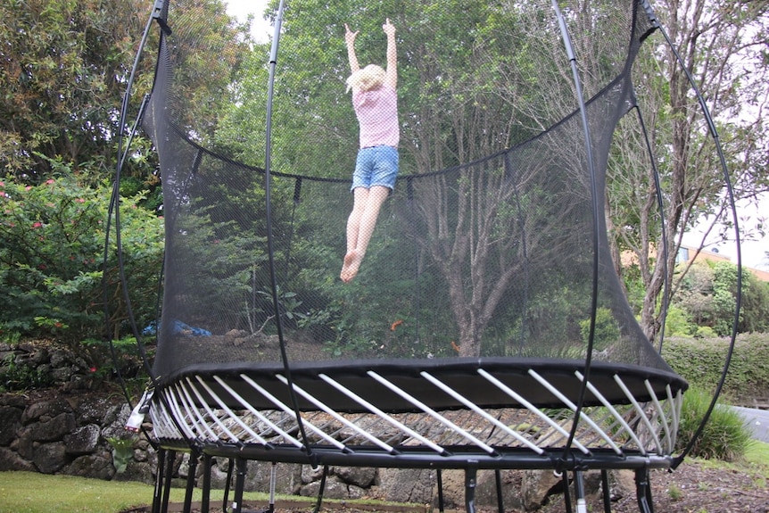A child jumping on a round trampoline surrounded by a net.