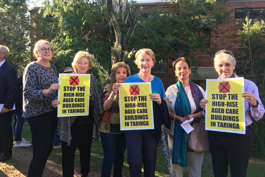 Six older women hold signs protesting a Tri-Care development in Taringa.