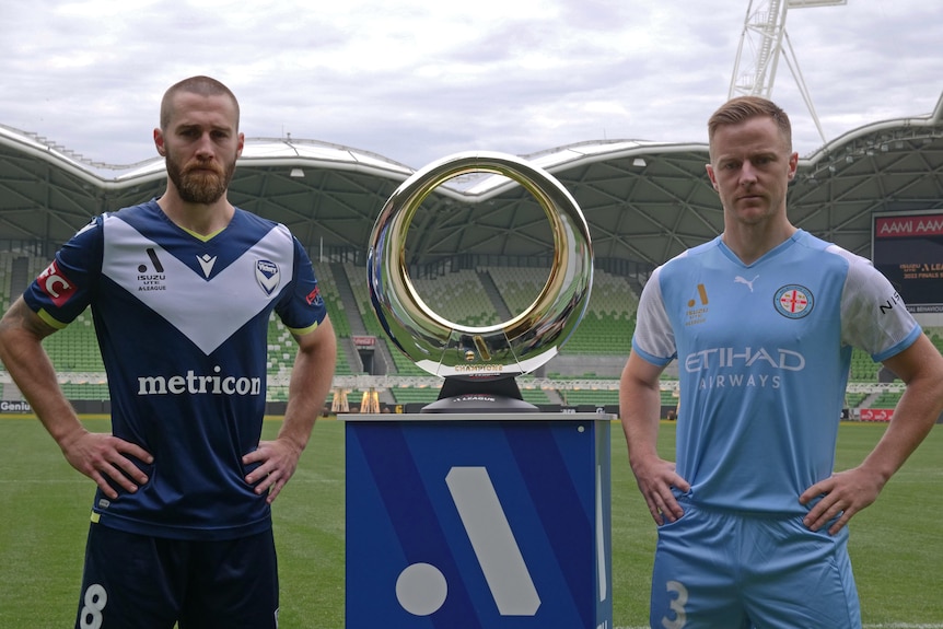 A-League captains Josh Brillante (left) and Scott Jamieson (right) stand either side of the Champions trophy.