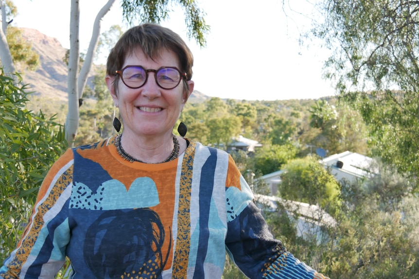 Professor Sue Kildea stands outside with a smile on her face. She is in Alice Springs and the township can be seen behind her.