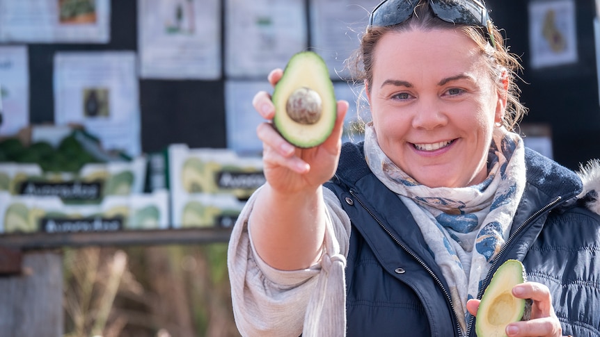 A woman holds out an avocado to camera.