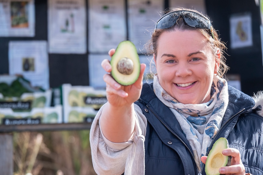 A woman holds out an avocado to camera.