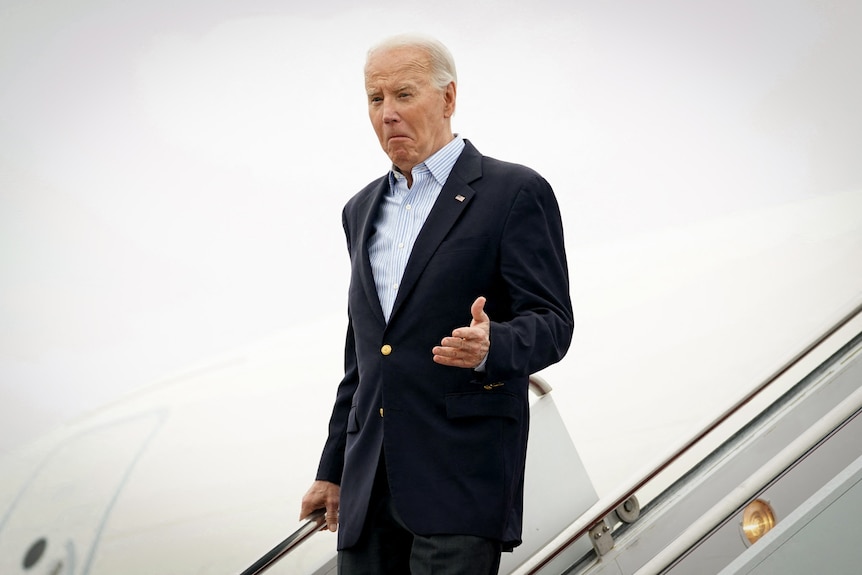 Joe Biden dressed in a suit hops off a plane and descend down some stairs.